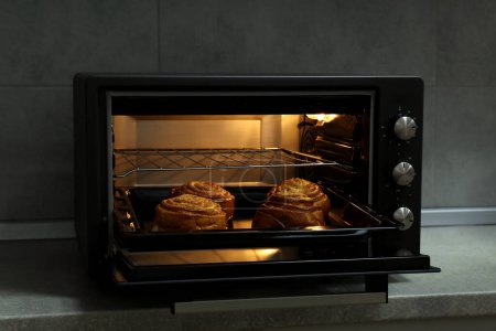 Open electric oven with delicious pastry on grey table indoors