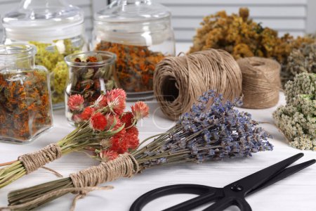 Photo for Bunches of dry flowers, different medicinal herbs, scissors and spools on white wooden table - Royalty Free Image