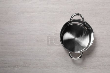 Photo for Empty steel pot on light wooden table, top view. Space for text - Royalty Free Image