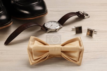Elegante corbata de lazo beige, zapatos, reloj de pulsera y gemelos sobre fondo de madera blanco