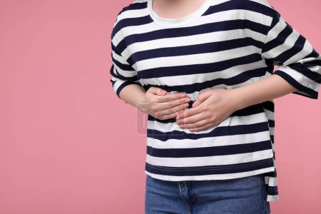 Foto de Mujer joven que sufre de dolor de estómago en el fondo rosa, primer plano. Espacio para texto - Imagen libre de derechos
