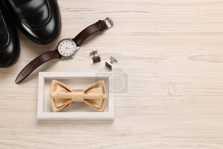 Elegante corbata de lazo beige, zapatos, reloj de pulsera y gemelos sobre fondo de madera blanca, posición plana. Espacio para texto