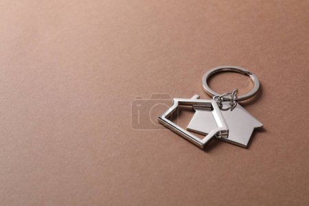 Téléchargez les photos : Porte-clés métalliques en forme de maisons sur fond brun clair. Espace pour le texte - en image libre de droit