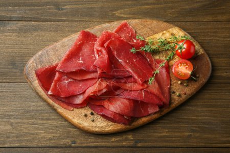 Photo for Tasty bresaola, peppercorns, tomatoes and thyme on wooden table, top view - Royalty Free Image