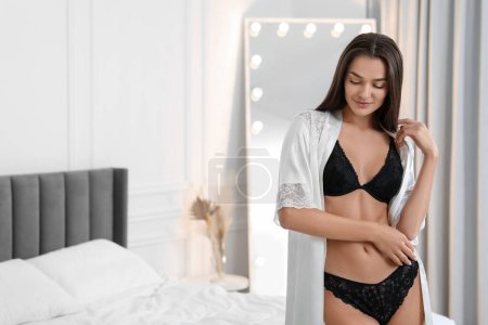 Photo for Young woman in elegant black underwear and robe indoors. Space for text - Royalty Free Image