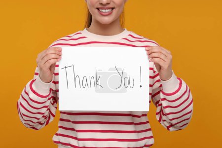 Woman holding card with phrase Thank You on orange background, closeup