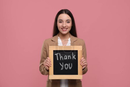 Glückliche Frau hält kleine Kreidetafel mit dem Satz "Danke" auf rosa Hintergrund