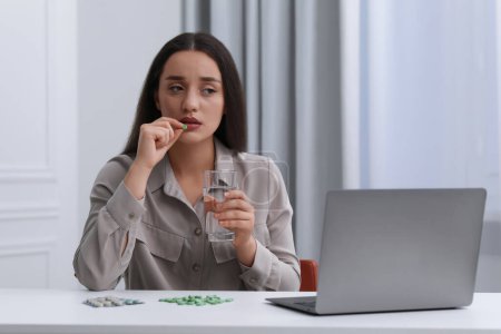 Foto de Mujer deprimida con vaso de agua tomando píldora antidepresiva en la mesa blanca en el interior - Imagen libre de derechos