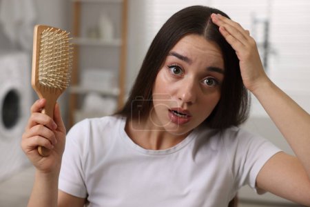 Téléchargez les photos : Femme émotionnelle avec brosse examinant ses cheveux dans la salle de bain. Problème de pellicules - en image libre de droit