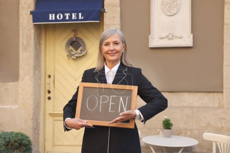 Photo for Happy business owner holding open sign near her hotel outdoors - Royalty Free Image
