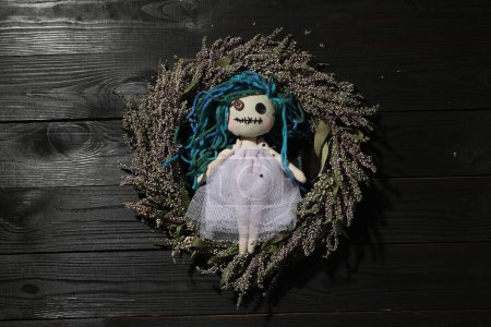 Weibliche Voodoo-Puppe mit Anstecknadeln und Kranz auf schwarzem Holzhintergrund, Draufsicht
