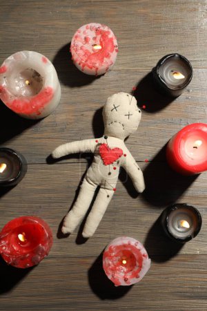 Voodoo-Puppe mit Stecknadeln im Kreis brennender Kerzen auf Holztisch, flach gelegt