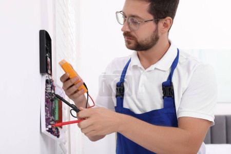 Foto de Técnico que utiliza multímetro digital mientras instala el sistema de alarma de seguridad doméstica en la pared blanca en interiores - Imagen libre de derechos
