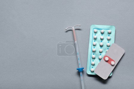 Pastillas anticonceptivas y dispositivo intrauterino sobre fondo gris claro, disposición plana y espacio para el texto. Elección del método anticonceptivo