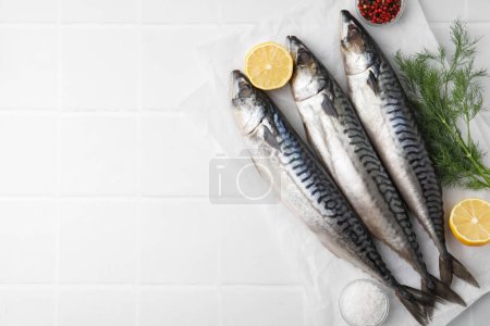 Tasty salted mackerels, spices and cut lemons on white tiled table, flat lay. Space for text