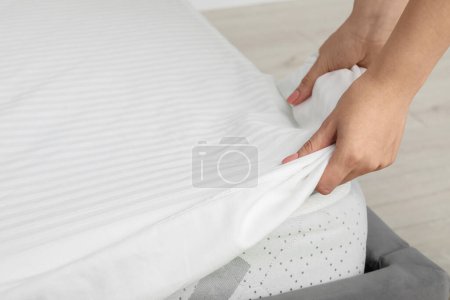 Woman putting cover on mattress indoors, closeup
