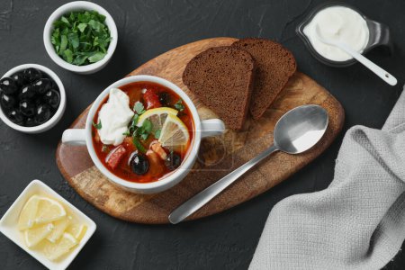 Meat solyanka soup with sausages, olives and vegetables served on dark grey textured table, flat lay