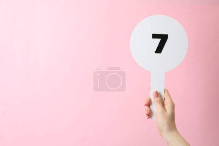 Femme tenant vente aux enchères pagaie avec le numéro 7 sur fond rose, gros plan. Espace pour le texte