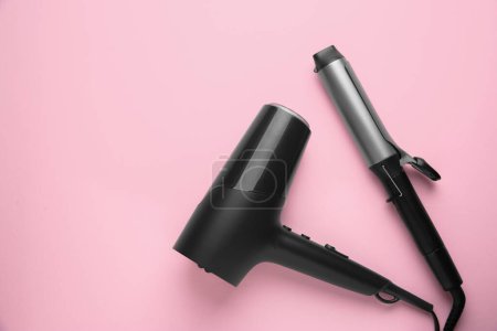Hair dryer and curling iron on pink background, top view. Space for text