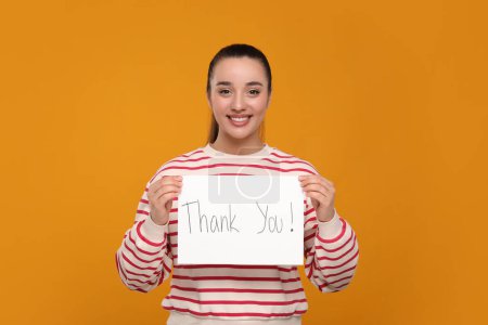 Feliz mujer sosteniendo tarjeta con frase Gracias sobre fondo naranja