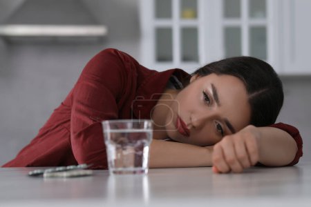Foto de Mujer deprimida en la mesa de mármol blanco con píldoras antidepresivas y vaso de agua en el interior - Imagen libre de derechos