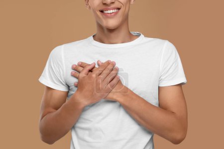 Thank you gesture. Grateful man with hands on chest against brown background, closeup