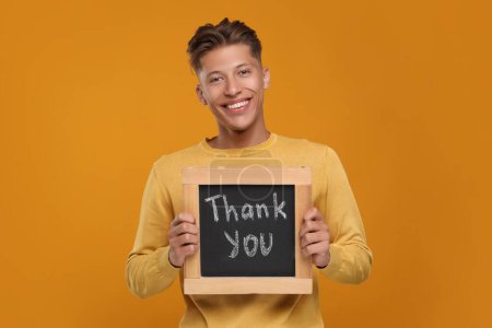 Homme heureux tenant petit tableau avec phrase Merci sur fond orange