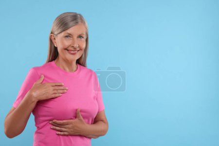 Belle femme âgée faisant l'auto-examen du sein sur fond bleu clair, espace pour le texte