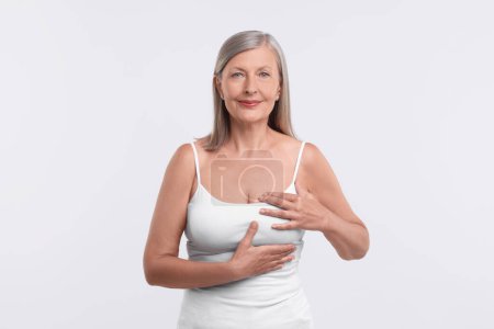 Beautiful senior woman doing breast self-examination on white background