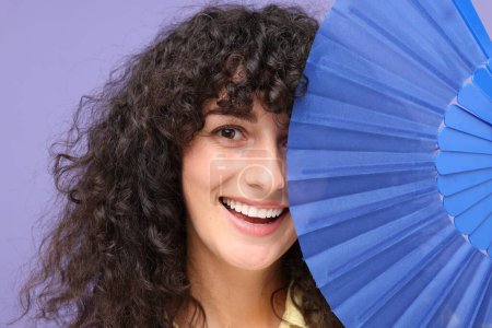 Foto de Mujer feliz sosteniendo ventilador de mano cerca de su cara sobre fondo púrpura - Imagen libre de derechos