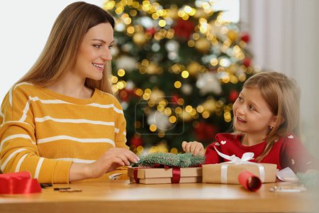 Christmas presents wrapping. Mother and her little daughter decorating gift box with fir tree branch at home