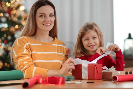 Geschenkpapier zu Weihnachten. Mutter und ihre kleine Tochter dekorieren Geschenkbox mit Schleife zu Hause