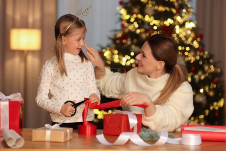 Envoltura de regalos de Navidad. Madre y su hija pequeña decorando caja de regalo con cinta en casa