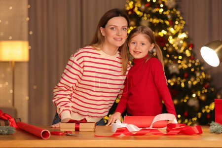 Envoltura de regalos de Navidad. Madre y su hija pequeña en la mesa con cajas de regalo, decoración en la habitación