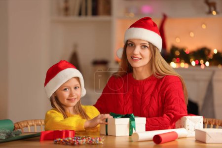 Envoltura de regalos de Navidad. Madre y su hijita con caja de regalo a la mesa en la habitación