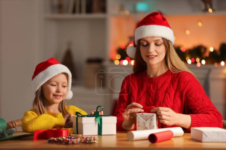 Envoltura de regalos de Navidad. Madre y su hija pequeña decorando cajas de regalo con cinta en casa