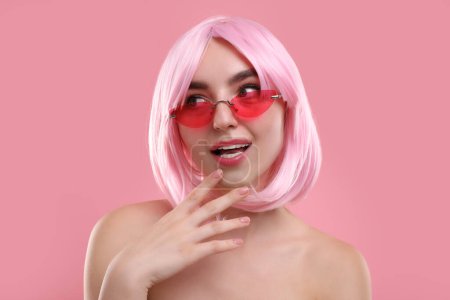 Pink look. Beautiful girl in wig and bright sunglasses on color background