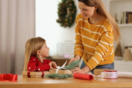 Geschenkpapier zu Weihnachten. Mutter und kleine Tochter schmücken Geschenkbox zu Hause mit Tannenzweig