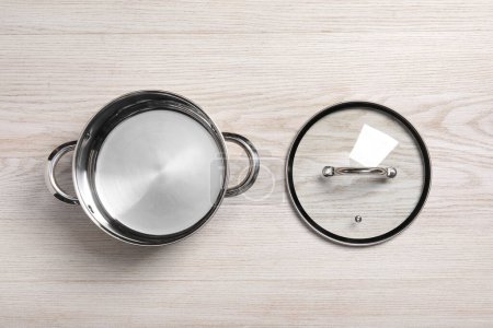Steel pot and glass lid on white wooden table, flat lay