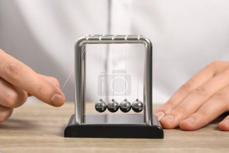 Photo for Man playing with Newton's cradle at wooden table, closeup. Physics law of energy conservation - Royalty Free Image