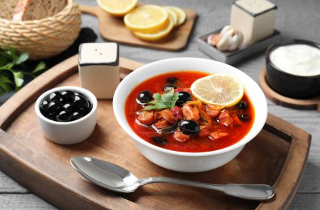 Fleischsoljanka-Suppe mit Würstchen, Oliven und Gemüse in Schüssel auf grauem Tisch