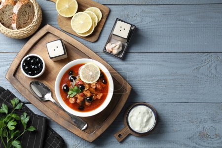 Meat solyanka soup with sausages, olives and vegetables served on grey wooden table, flat lay. Space for text