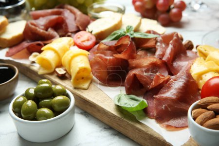 Photo for Charcuterie board. Delicious bresaola, olives, tomato, cheese and almond on white marble table, closeup - Royalty Free Image