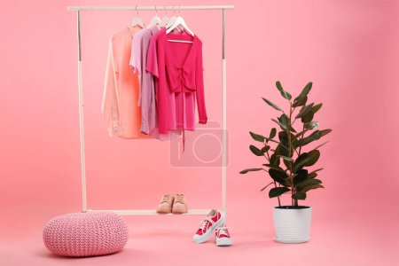 Support avec différents vêtements élégants pour femmes, baskets et plantes vertes sur fond rose