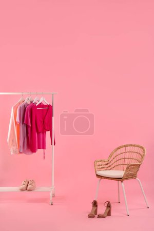 Support avec différents vêtements, chaussures et fauteuils élégants pour femmes sur fond rose