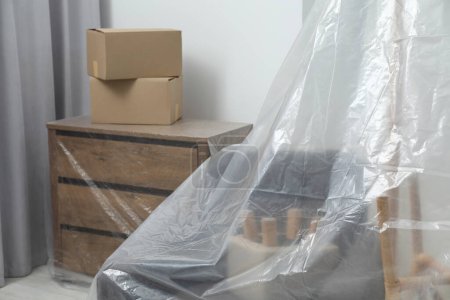 Foto de Muebles modernos cubiertos con película de plástico y cajas en casa - Imagen libre de derechos