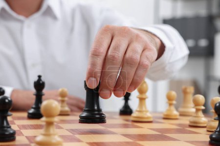 Man with rook game piece playing chess at checkerboard indoors, closeup