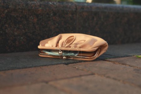 Beige leather purse on pavement outdoors, closeup. Lost and found