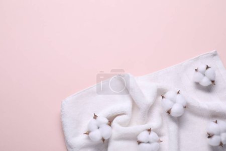 Flauschige Baumwollblumen und weißes Frottee-Handtuch auf beigem Hintergrund, Draufsicht. Raum für Text