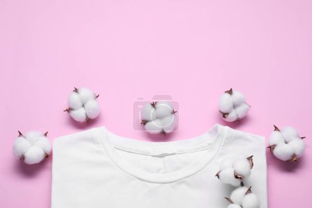 Flores de algodón esponjosas y camiseta blanca sobre fondo rosa, plano. Espacio para texto